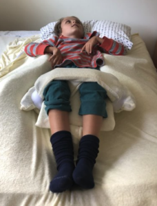 A child lying in a bed, supported by therapeutic pillows that keep their body in position