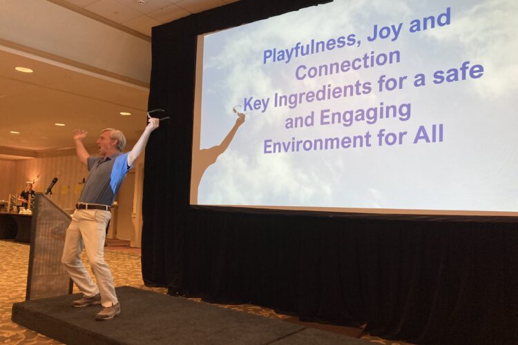 A jubilant white man gestures broadly in front of a screen