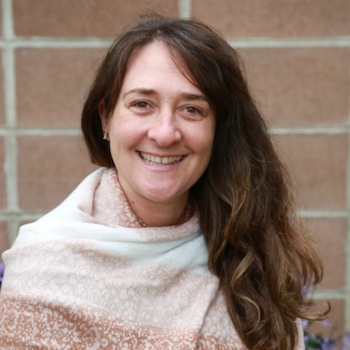 Julia Wayne: a peach-skinned woman with long brown hair, wearing a cream shawl smiles for the camera