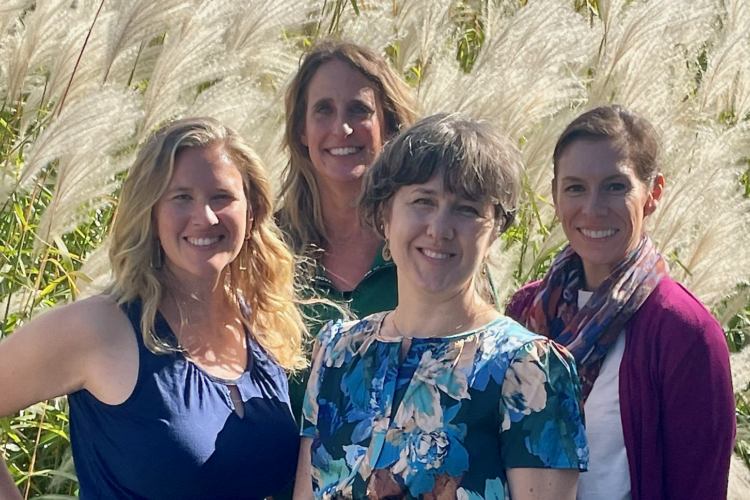 Picture of four white women standing in front of tall grasses and smiling.