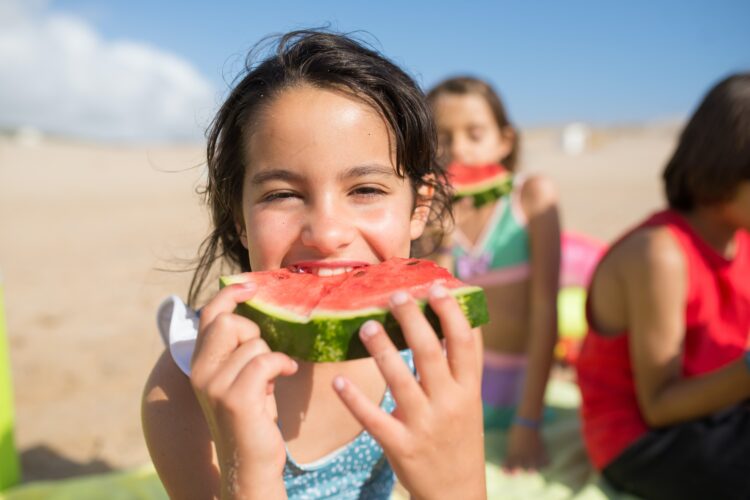 A pre-teen girl enjoying a slice of watermelon in the sun with friends