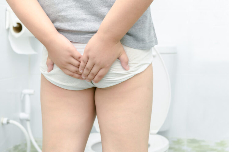 A small pale-skinned boy clutches at his diaper in front of a toilet