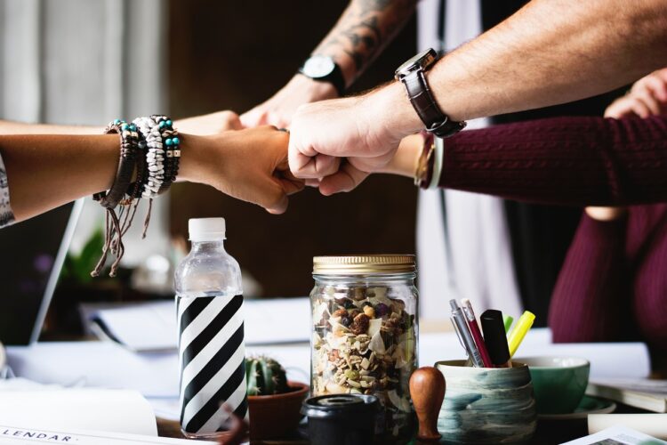 A group of hands together in the center of a crowded table in a show of teamwork