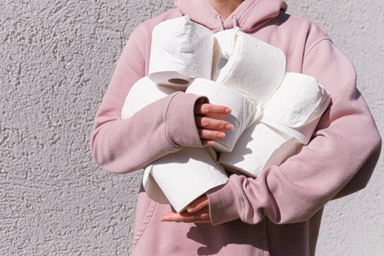 a person in a pink hoodie clutches many, many toilet rolls