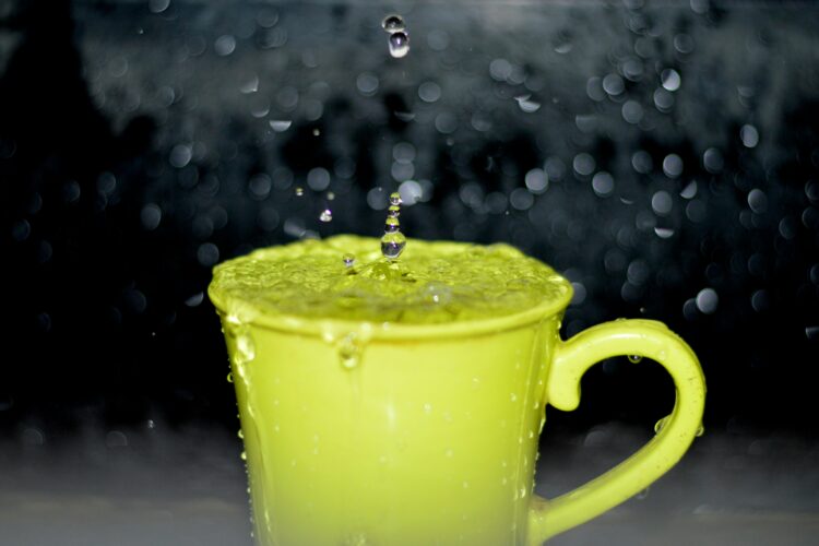 A yellow cup is over-filled with water as it sits out in the rain