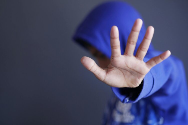 A child in a hoodie turns their face away from the camera and holds up a hand in the international "no" symbol