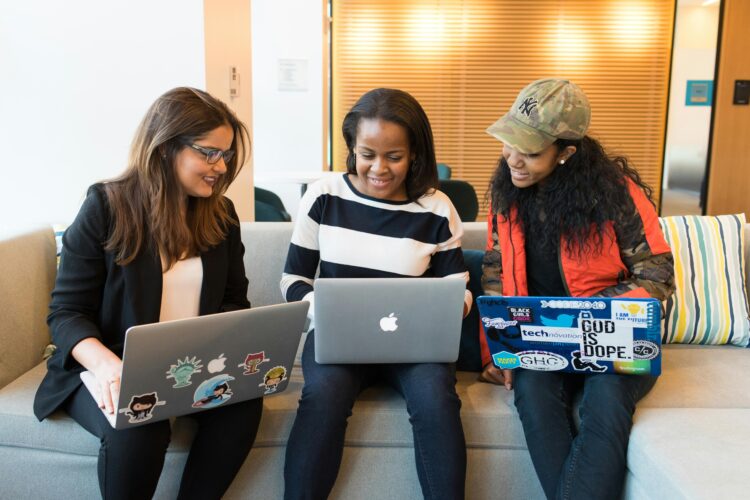 Three women peruse open laptops