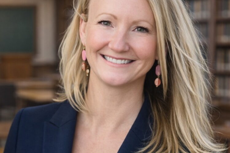 A white woman with straight blonde hair worn loose to her shoulders, smiling happily at the camera.