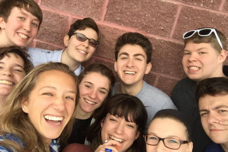 A group of college-aged people pose for a selfie against a brick wall