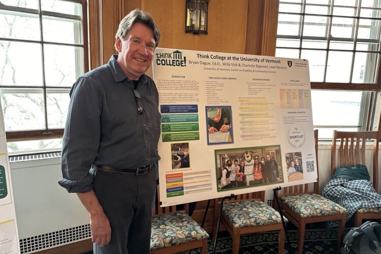 A ruddy-skinned man in his sixties with thick short walnut-brown hair poses for a photo next to a research poster mounted on an easel