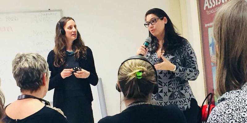 A pair of women stand and address seated students in a lecture hall