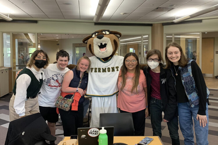 a group of college-aged students, some with visible disabilities, some without, pose for photo with the UVM mascot, a catamount in a basketball uniform