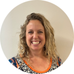 A white woman in her mid-thirties with curly blonde hair worn loose to her shoulders, smiling happily at the camera