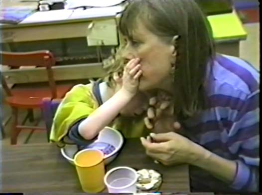 Figure 13a. A DeafBlind kindergartner and a woman are eating a snack side by side.
The woman is chewing a cookie as the kindergartner reaches up to feel her mouth as
she chews. The concept being developed might be, “Other people eat, too, and enjoy
eating.” Being blind, he might not know that other people eat. He also might not have a
model of table manners if he doesn’t have a partner willing to show him.