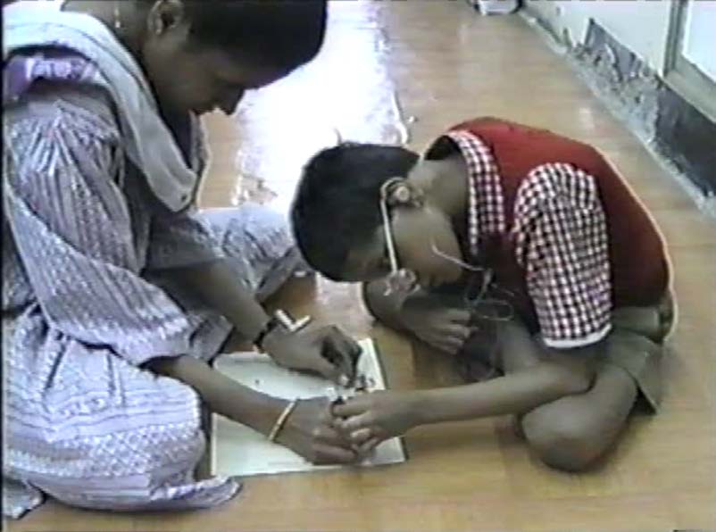 Figure 14b: Later on, the teacher drew the ring by placing it on a piece of paper. The
boy joined in, placing his hand on hers as she drew. He also felt the motions of writing
as she wrote the word “ring” on the paper. Body memory is part of learning. This boy
may be developing concepts such as, “My teacher is interested in rings, too,” and
“Drawing and writing are fun.” The picture of the ring and the word that names it became
a part of a shared memory book that the teacher and the boy can refer back to regularly.