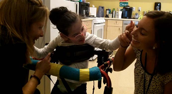 Figure 15a. Two teachers include a student in a supportive walker as they go together
from one activity to the next. They support the student to interact at her own comfortable
pace. The teachers are kneeling down, positioned at the student’s eye level. This is a
child-centered interaction.