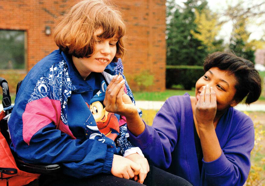 Figure 1b. The intervener has imagined that the girl might be interested in smelling the
flowers, so she picks a flower and they begin their conversation by smelling the flower
together. Their smiles confirm their mutual enjoyment. The intervener is signing the
word “flower” as part of the conversation.