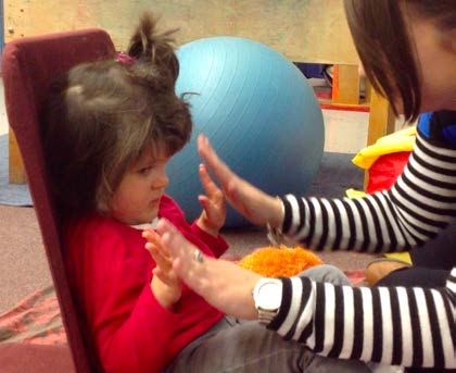 Figure 2b. The young girl and her intervener continue in the same position on the floor
and bring their hands together to pat each others’ hands. The girl shifts her eyes to the
right to peek at her hands as they touch the intervener’s.