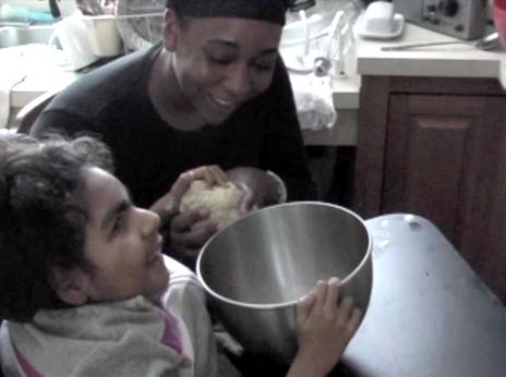 Figure 3a. A teenager and her partner are participating in a shared experience of
making bread. The partner is holding the bread dough in her hands and using natural
language to talk about what they’re doing. The teenager is reaching out and touching the
dough with her left hand while holding the bowl with her right hand. The teenager and
her partner are both smiling as they touch the bread dough together.