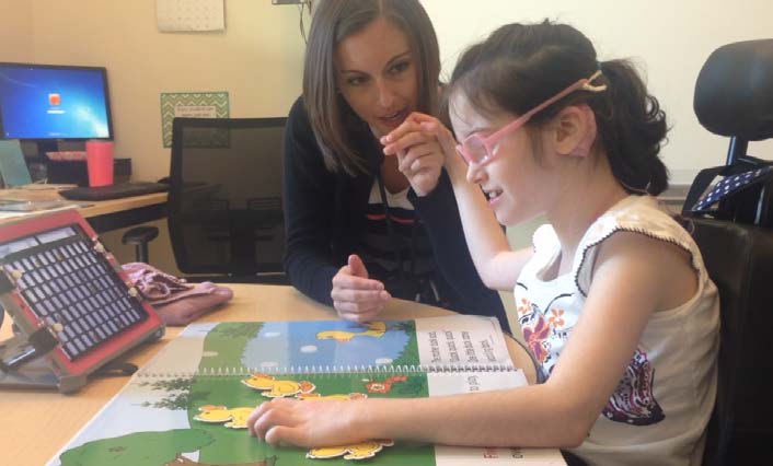 Figure 6a. A speech-language pathologist supports a child’s exploration of an adapted
book by signing into her right hand. The child follows the book visually and with her left
hand at the same time. This contact with the girl will give her partner the opportunity to
notice when the girl seems delighted, and sign the words, “I see you like that!” at that
moment.