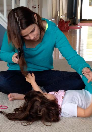 Figure 7a. This girl doesn’t yet know how to brush her own hair. She has very limited
vision and hearing. So her mother is leaning in closely as the daughter lies on the floor
and reaches her left hand up to touch her mother’s hair, feeling it move as her mother
brushes it.