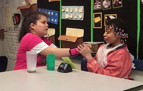 Figure 8a & 8b. A teacher facilitates peer-to-peer interactions, modeling for one student
how to support another student with hand under hand signing, to request “more drink.”