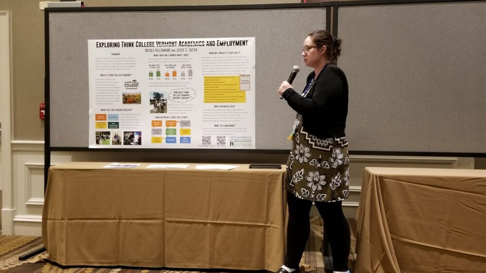 a pale-skinned college-aged woman speaks into a microphone in front of a research poster