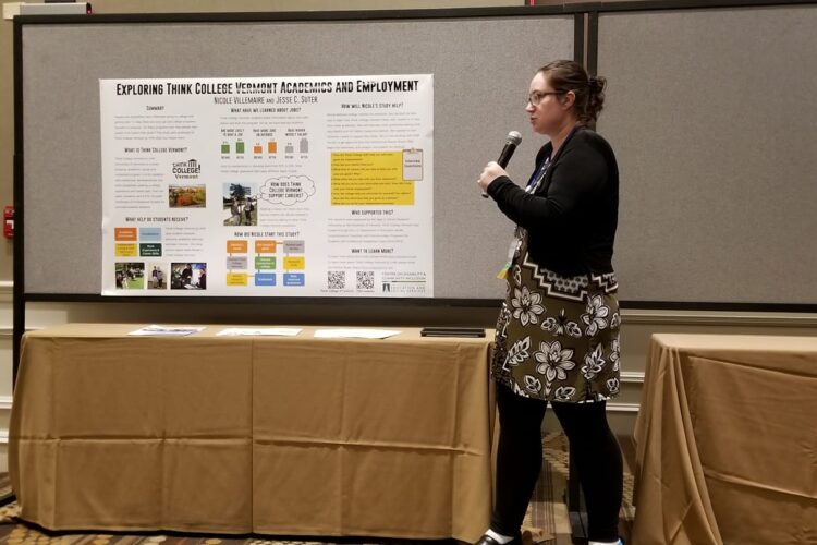 a pale-skinned college-aged woman speaks into a microphone in front of a research poster