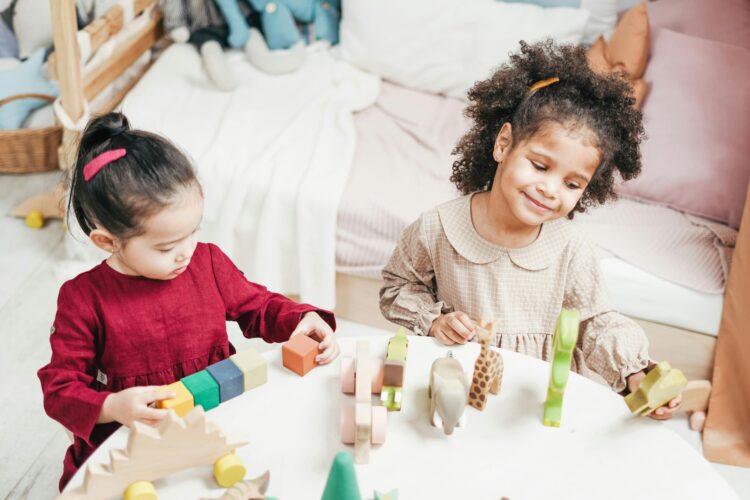 Two toddler girls play with toys at a low table