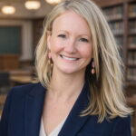 A white woman with straight blonde hair worn loose to her shoulders, smiling happily at the camera.