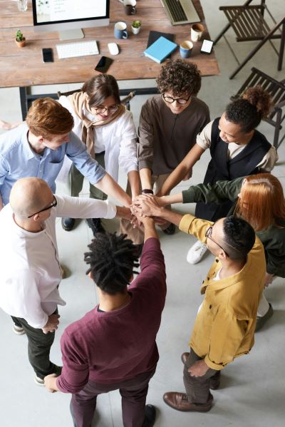 A group of 8 young professionals stand in a circle with their hands joined in the middle
