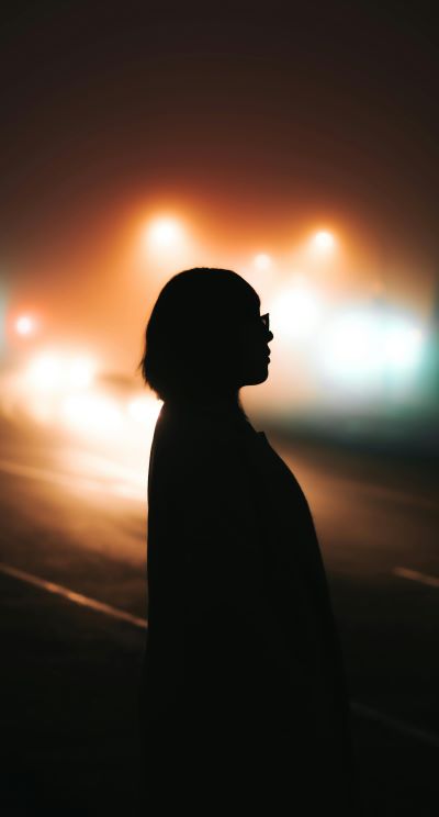 Silhouette of Person Standing on Road against colorful blurry city lights during Night Time