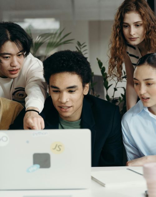 4 young professionals huddled around lap top in a work environment