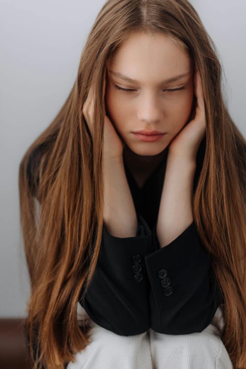 Portrait of young person with closed eyes and long auburn hair covering ears with hands